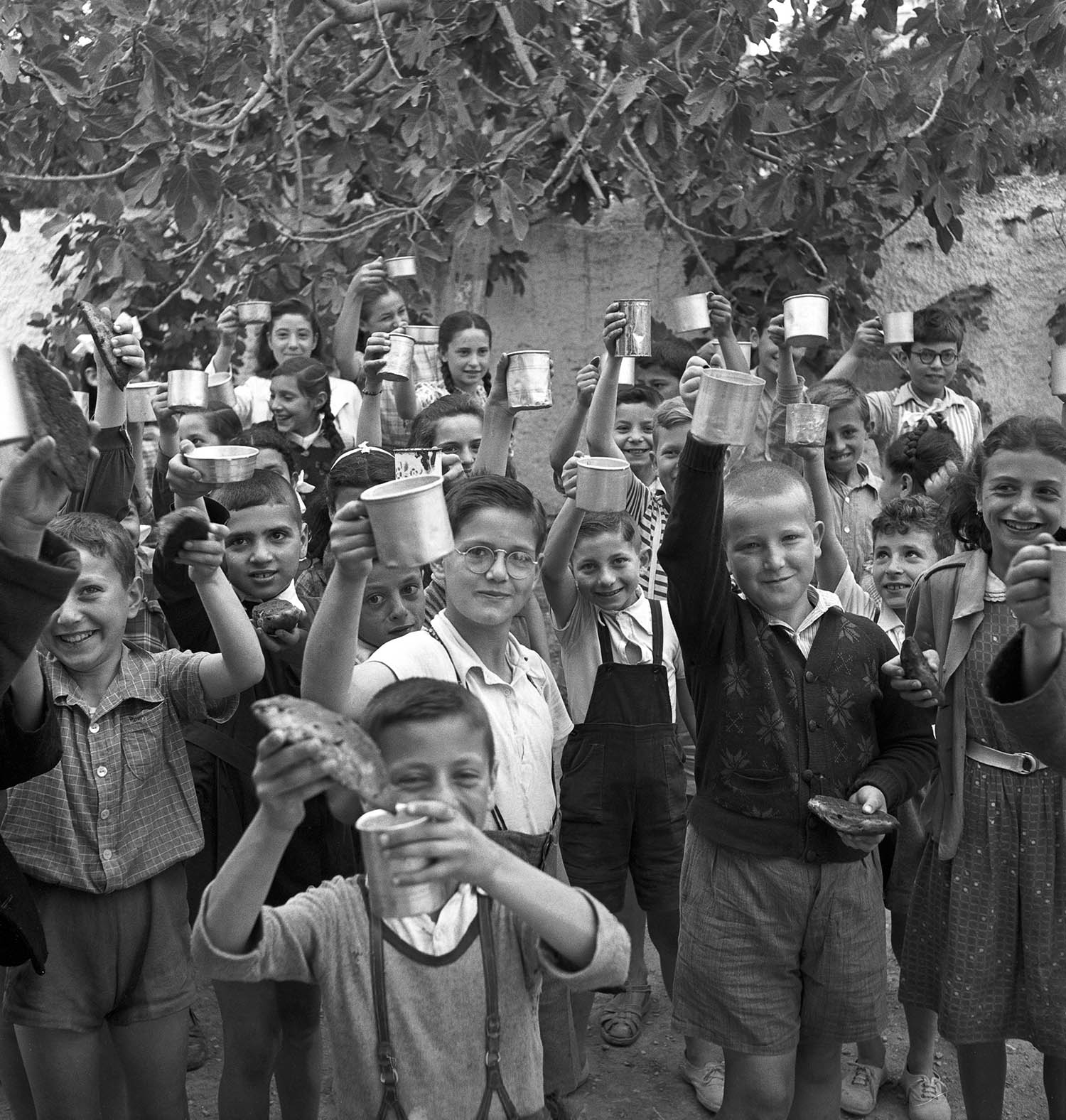 Greek schoolgirls and schoolboys smile as they hold up bread rolls and tin mugs