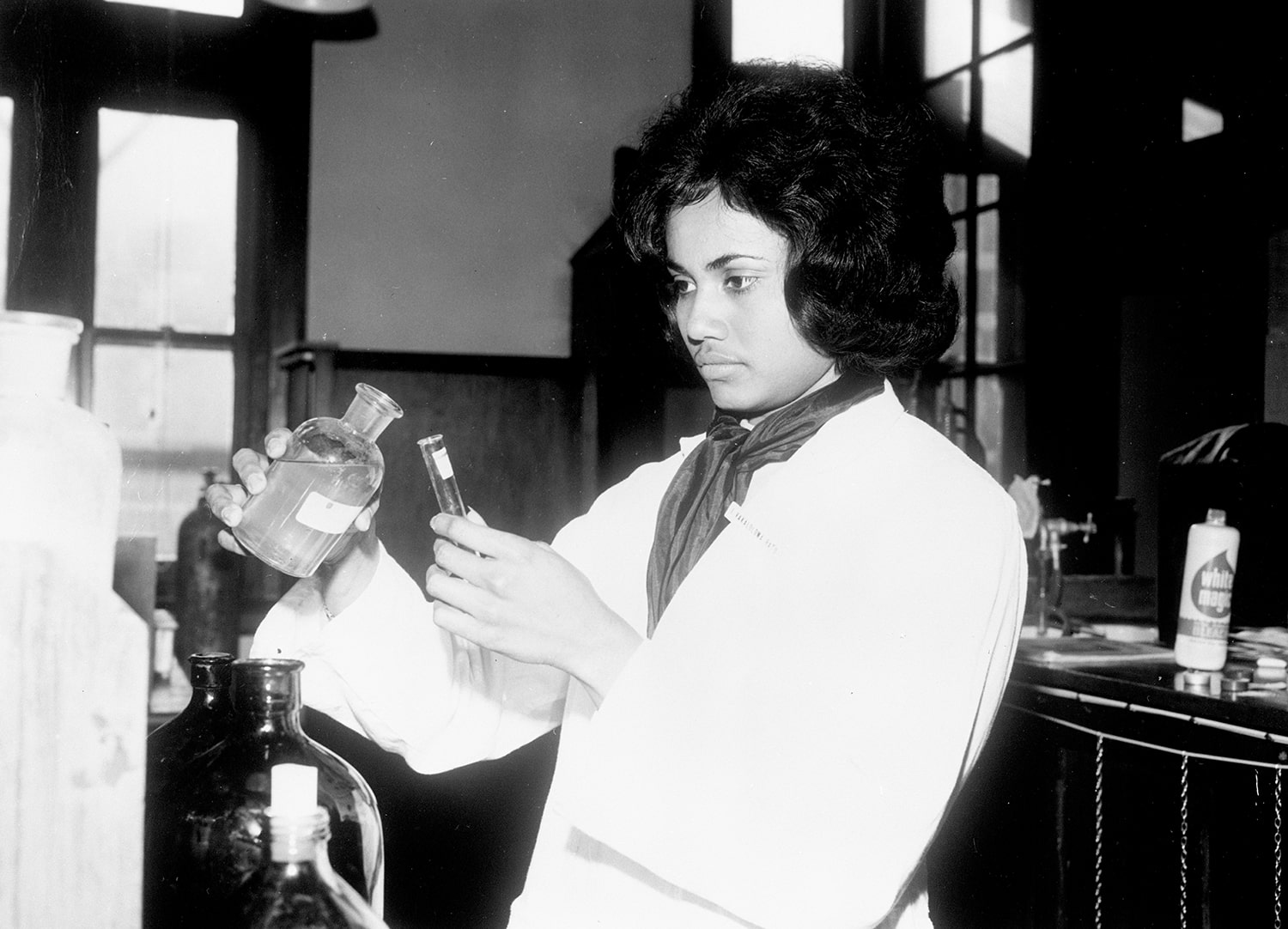 A young Fijian woman in a lab coat pours liquid into a test tube