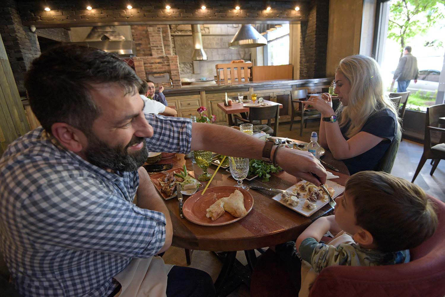 An Armenian family (mother, father and child) enjoy a meal out in a bright-lit restaurant