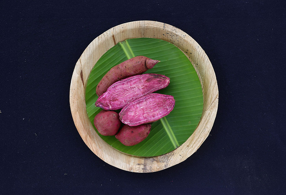 Biofortified sweet potatoes, some cut with purple flesh showing, sit in a round wooden dish