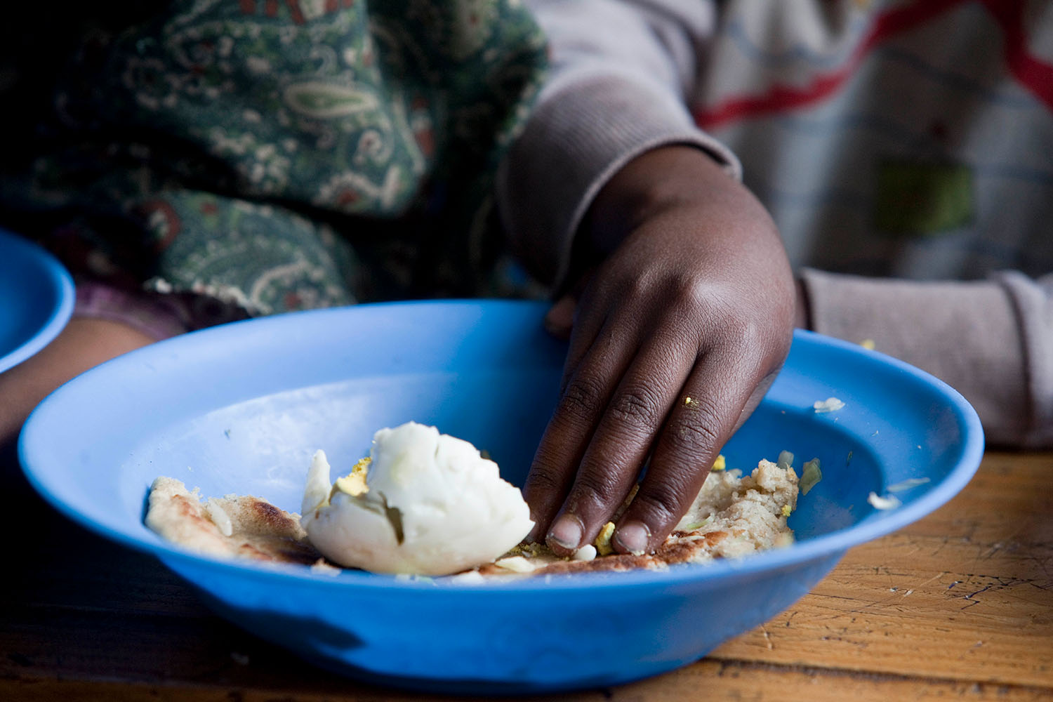 Close-up of an African boy's hand scooping food out of a blue plate